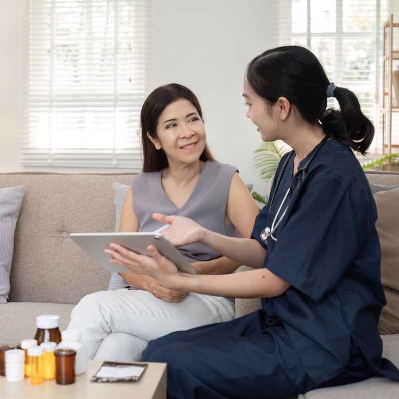 Nurse explains her notes to a patient while sitting in her couch at home.