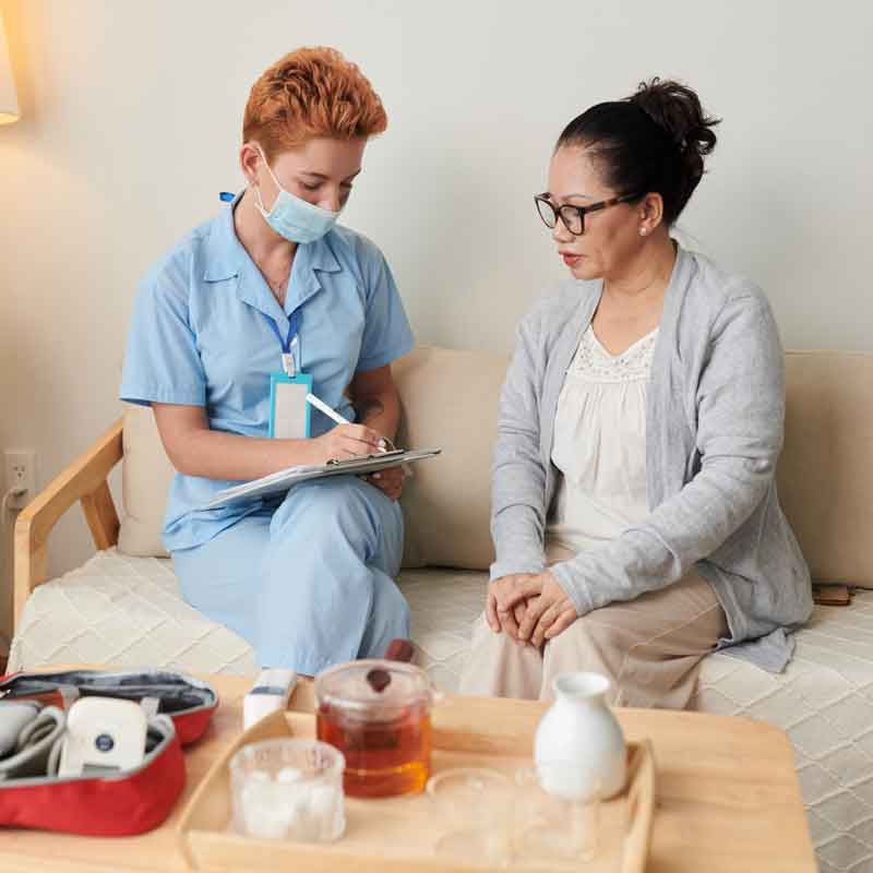 Nurse with patient sitting on a couch in the patient's home.