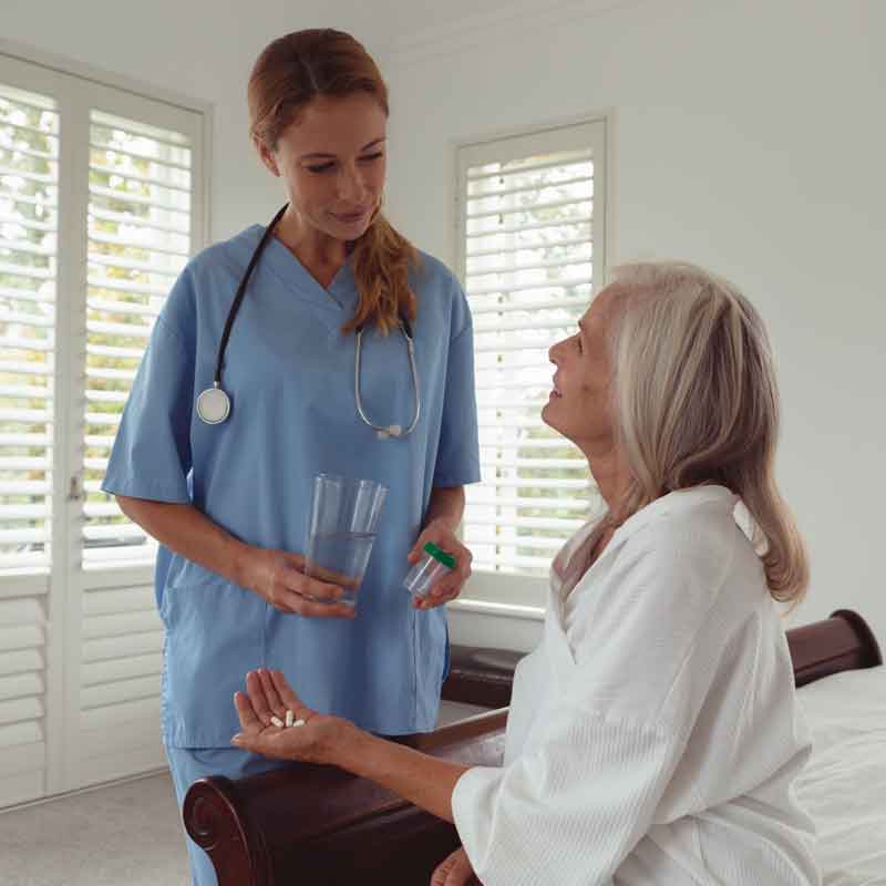 Nurse standing next to patient resting in her bed at home.